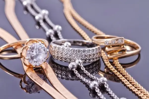 A macro shot of an assortment of gold-plated and silver jewelry, including rings with gemstones and various chain styles, on a reflective surface.