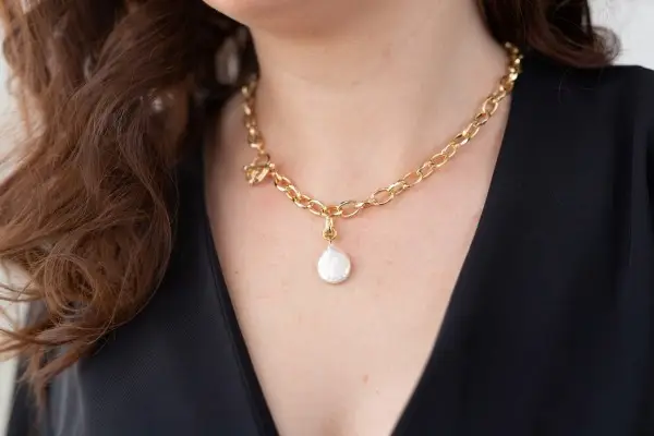A woman wearing a stylish gold-plated link necklace that features an elegant, dangling pearl pendant.