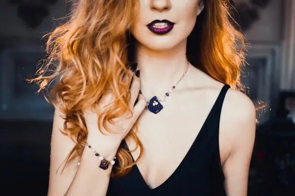A woman with dark lipstick models a gothic-style necklace and bracelet set with deep purple gemstones, showcasing a perfect jewelry style for a witchy Halloween costume.