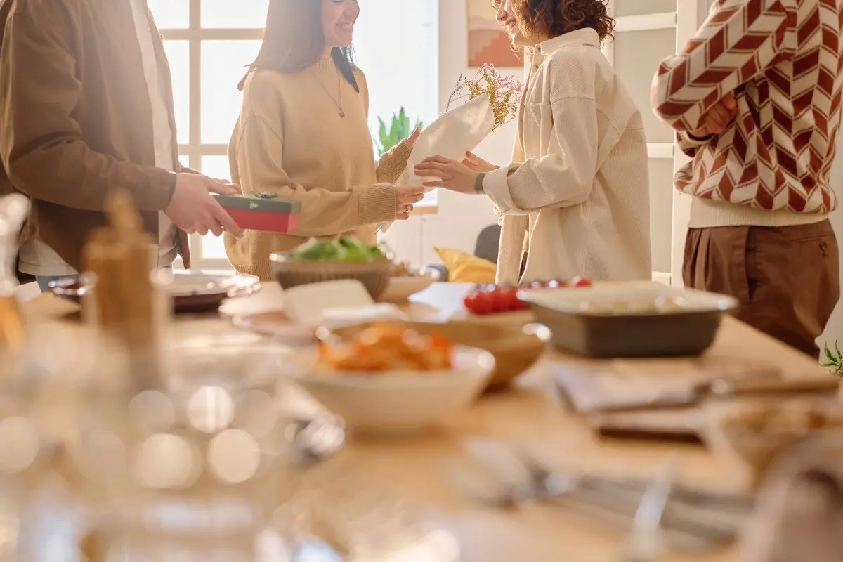 A hosuewarming party showing people exchanging gifts and serving food at a dinner table.