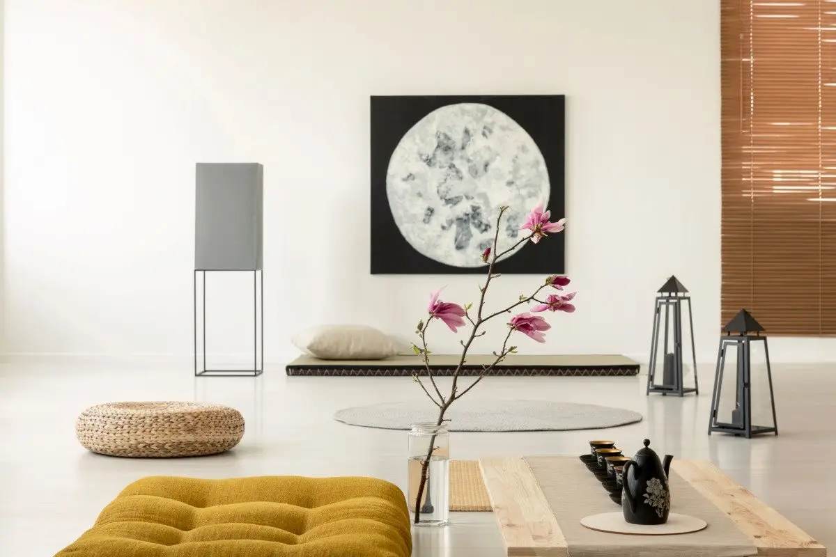A serene and minimalist modern Japanese living room featuring a low-profile grey sofa, a simple round wooden coffee table, and a large window with a view of green foliage, embodying Wabi-sabi principles.