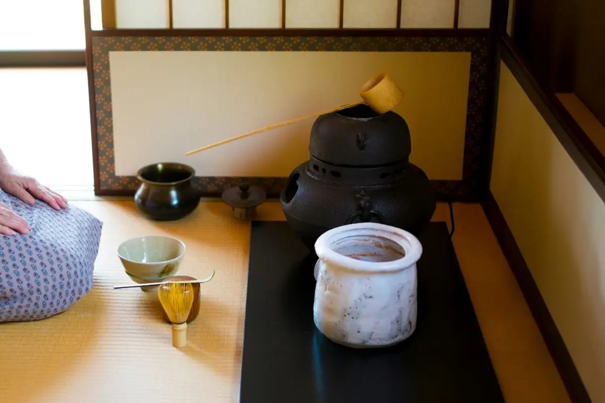 A perfect example of Wabi-sabi decor: a rustic, imperfectly shaped ceramic vase holding a single dried branch against a textured, neutral-colored wall.