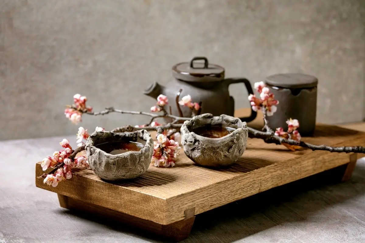 Thoughtful and functional Japanese decor, with a simple black cast-iron teapot and ceramic cups arranged neatly on a low wooden shelf.