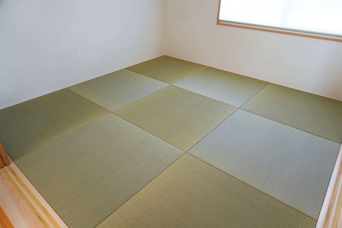 A traditional Japanese room corner with woven tatami mats on the floor, and a shoji screen window allowing soft light to enter.