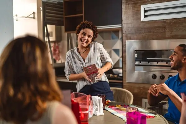 Brazilian friends sitting at a table and giving each other Christmas gifts.