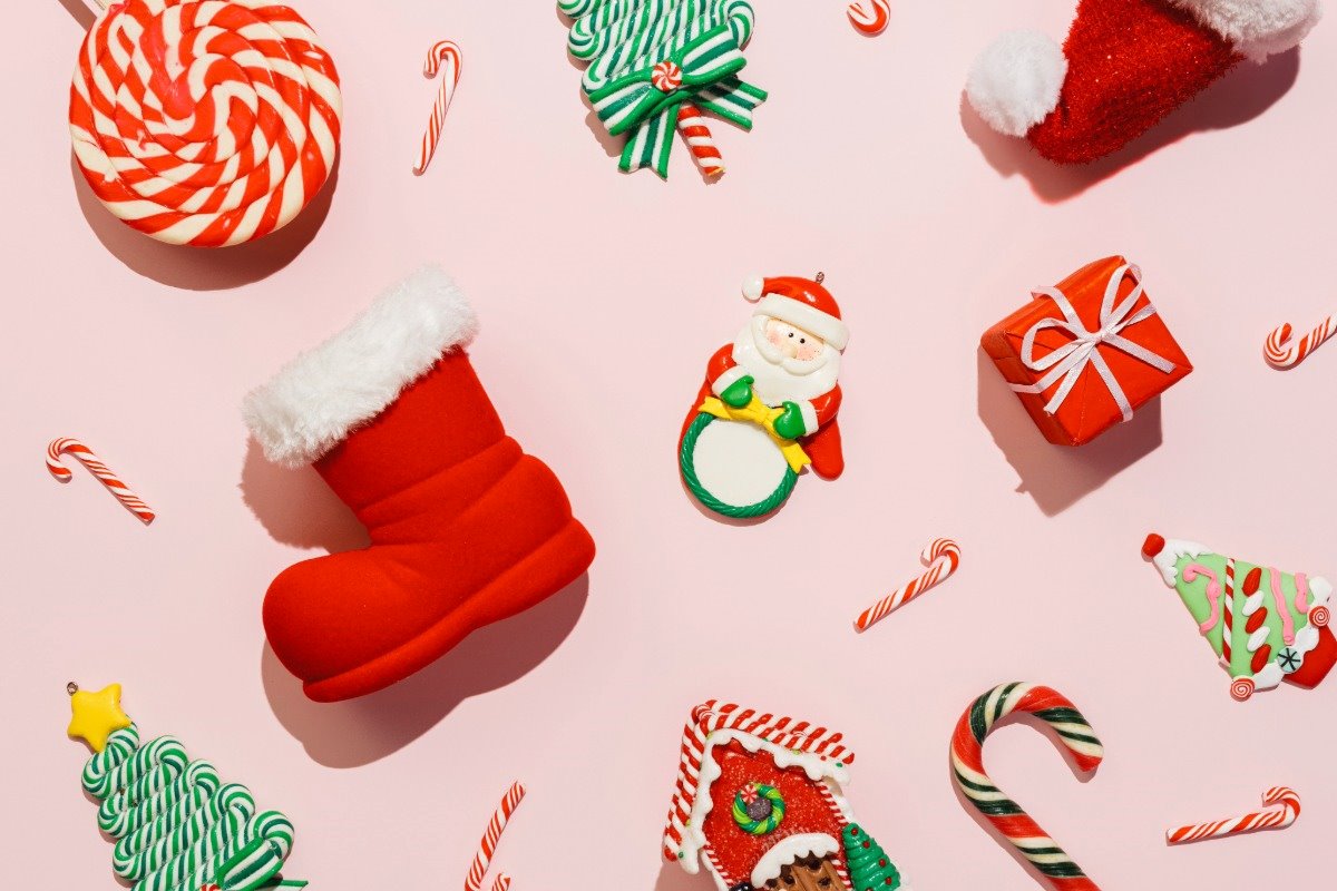 Red and white Christmas socks and Santa hats on a pink background with Christmas stocking stuffers.