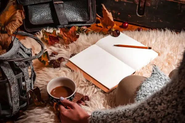 A person enjoying a mindful hygge moment, writing in a journal with a cup of hot chocolate on a cozy sheepskin rug.