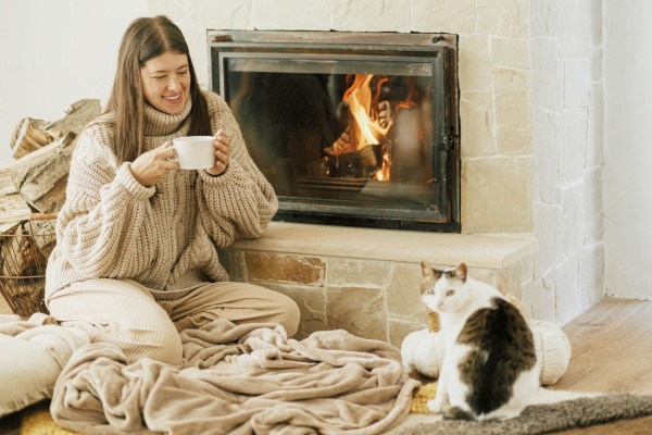 The ultimate hygge scene: a cat sleeping peacefully on a chunky knit blanket in front of a warm, crackling fireplace.