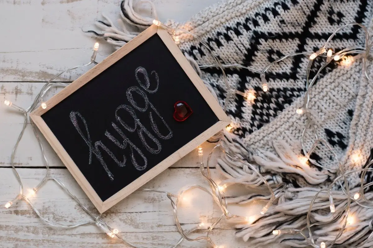 A small chalkboard with the word 'hygge' written in cursive, resting on a cozy Scandinavian knit blanket with warm fairy lights.