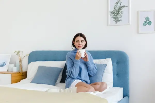 A woman in cozy blue pajamas enjoying a warm drink in bed, a perfect example of a personal hygge moment of comfort and relaxation.