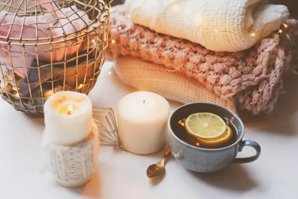 A quintessential hygge still life with lit candles, fresh bread in a basket, and a cozy knitted blanket, representing the warmth of Scandinavian comfort.