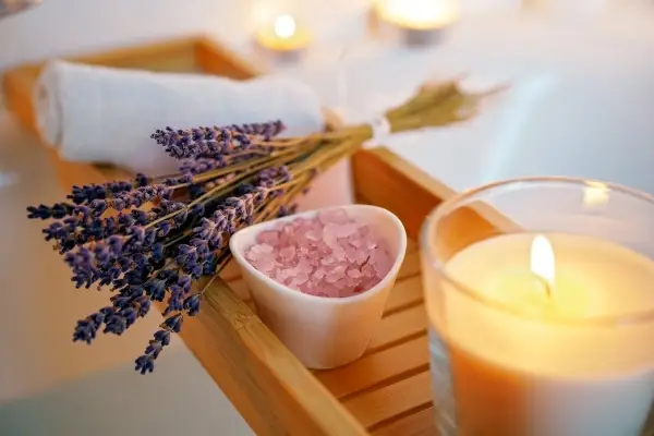 A relaxing self-care setup representing a perfect hygge gift, with a bowl of bath salts, fresh lavender, and lit candles.
