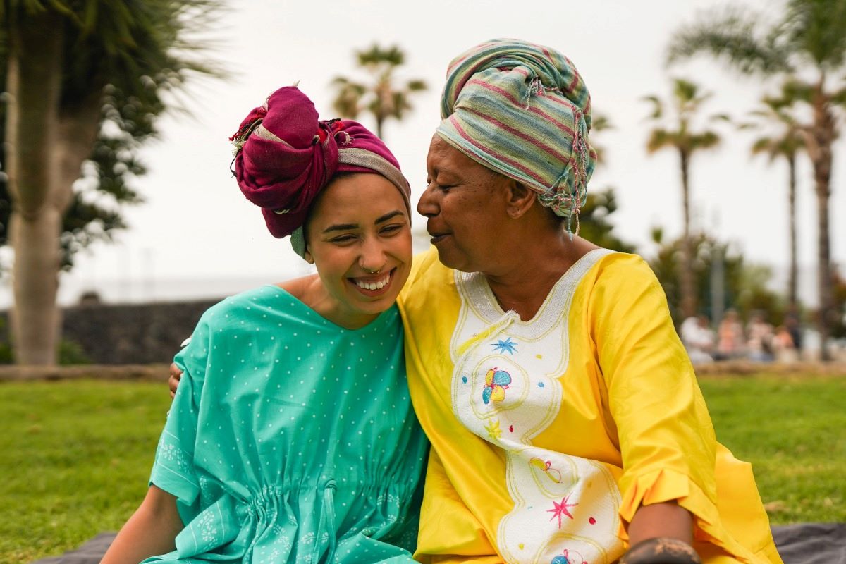 African mother's day, two smiling women: daughter and mother, wearing colorful traditional headwraps outdoors.