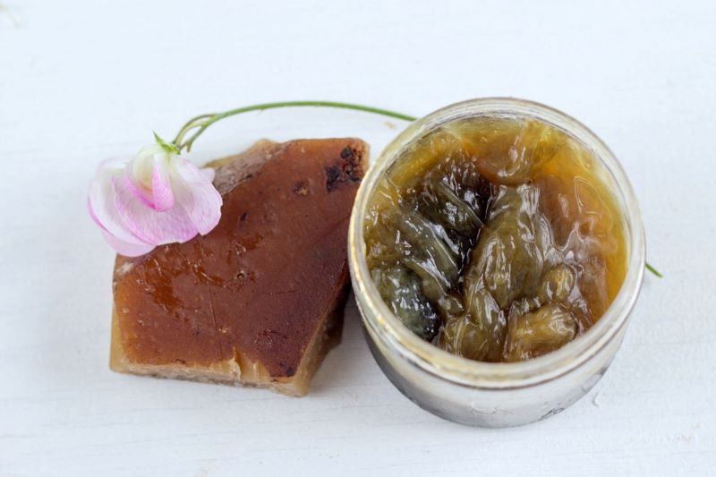 Natural black soap in a jar next to a rustic bar of black soap.