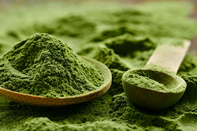 African qasil green herbal powder in a wooden spoon and bowl for natural skincare.