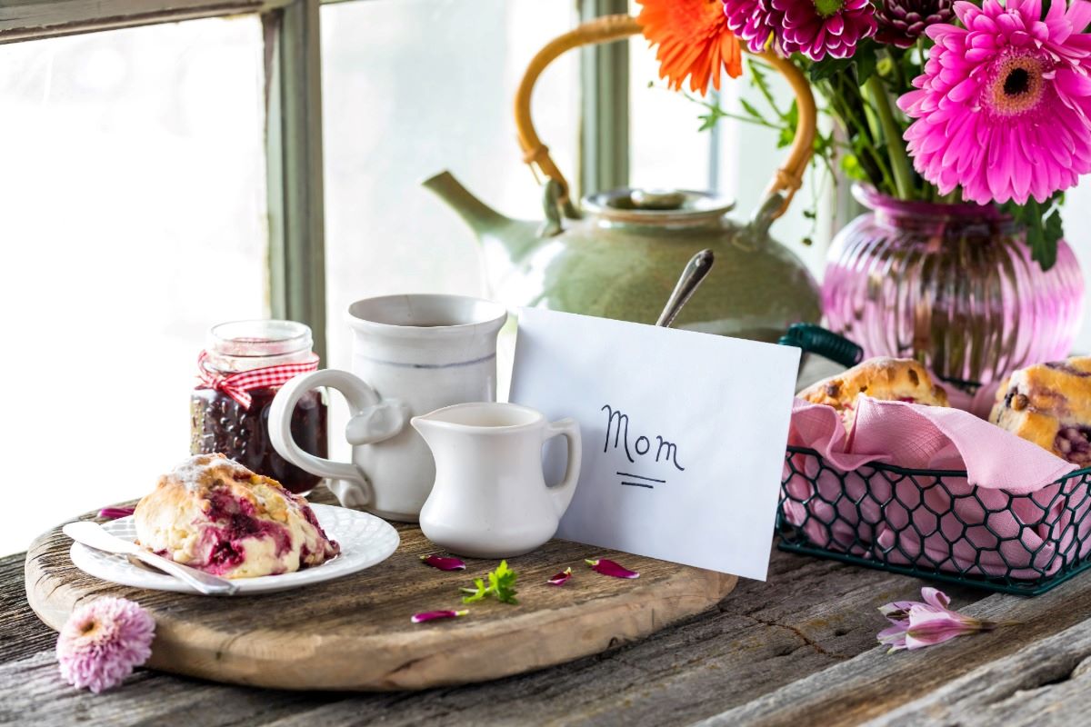 Cozy herbal tea setting on a wooden table near a window with a handwritten note for mother's day.