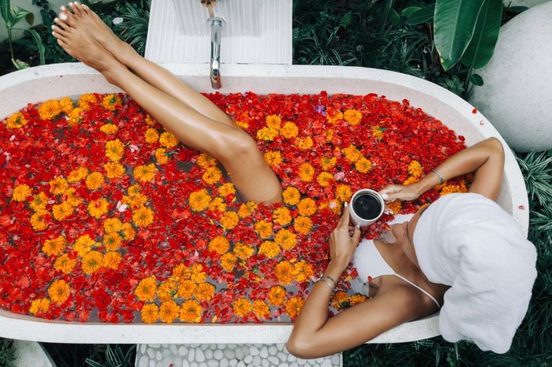 Top-down view of a woman relaxing in a spa bath filled with floating orange and red flower petals like in Bali retreat.