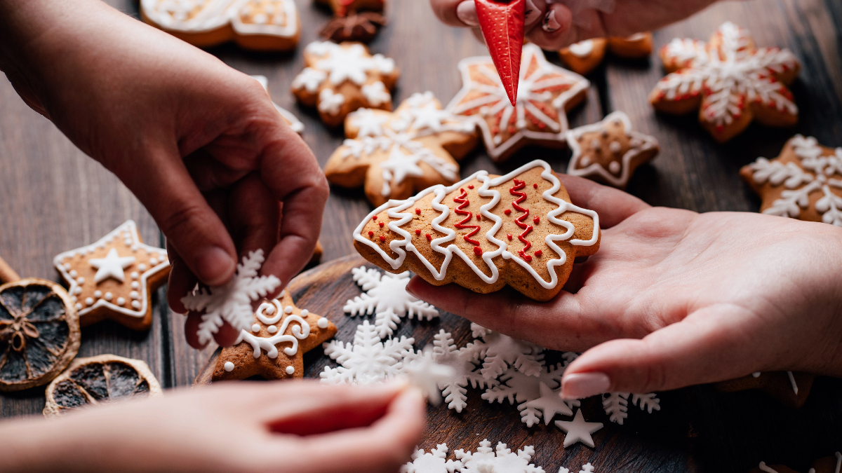 Mom's and daughter's hands holding freshly decorated, star-shaped gingerbread cookies with festive red and white icing.
